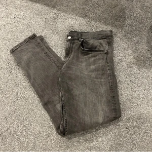 Grå jeans från J.Lindeberg - Snygga grå jeans från J.Lindeberg i en klassisk stil. De har en normal passform och är perfekta för en stilren look. Jeansen har en knapp och dragkedja framtill samt fem fickor.