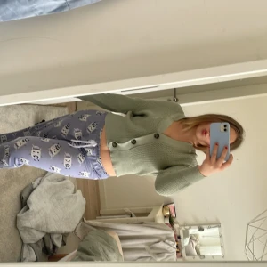 Grön ribbad kofta - Säljer en stilren grön ribbad kofta med knappar framtill. Koftan har en croppad passform och långa ärmar, perfekt för en trendig look. Passar bra till både jeans och kjol.