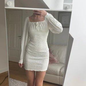 Vit klänning med smockdetaljer - Studentklänning. Jag är 175 cm. Xs/s. Säljer en söt vit klänning med smockdetaljer och långa ärmar. Klänningen har en åtsittande passform och en fyrkantig urringning. Perfekt för sommarens alla tillfällen!