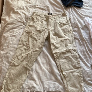 Beige linnebyxor från Only & Sons - Säljer ett par stilrena beige linnebyxor från Only & Sons. Byxorna har en normal passform och är perfekta för varmare väder. De har en klassisk design med knappar och dragkedja framtill.