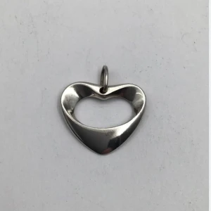 Silverfärgat hjärthänge George Jensen  - Elegant silverfärgat hänge i form av ett hjärta av George Jensen, med en slät och blank yta. Perfekt för att fästa på ett halsband och ge en stilren touch till din look.