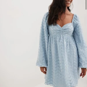 Ljusblå spetsklänning - Charmig ljusblå klänning i spets med v-ringad design och långa ärmar. Perfekt för sommaren. Den har en luftig passform.