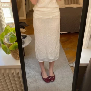 Vit prickig kjol - Säljer en vit kjol med små svarta prickar. Kjolen är knälång och har en normal passform. Perfekt för en stilren och klassisk look.