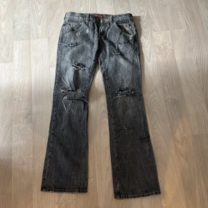 Grå jeans med slitningar - Snygga grå jeans med coola slitningar och broderade detaljer på bakfickorna. Står ingen storlek i men skulle säga att det är storlek 34 eller 36