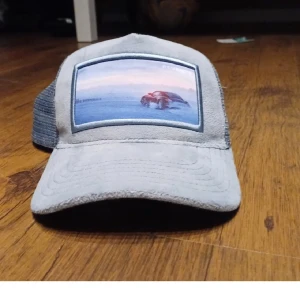 Grå keps med mesh och tryck - Snygg grå keps från Revenite med mesh-bakdel för bra ventilation. Framsidan har ett coolt tryck av en bil i snölandskap. Justerbar passform med knäppning bak.