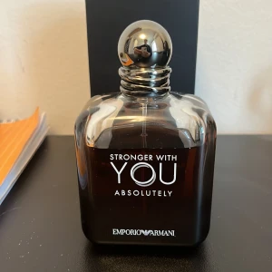 Stronger With You Absolutely från Emporio Armani - Säljer en elegant parfymflaska av Stronger With You Absolutely från Emporio Armani. Flaskan har en stilren design med en mörk ton och en metallisk kork. Perfekt för den som vill ha en sofistikerad doftupplevelse.