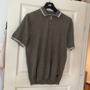 Grå kortärmad tröja från Bondelid - Säljer en stilren grå kortärmad tröja från Bondelid. Tröjan har en dragkedja framtill och en klassisk krage med vita ränder. Perfekt för en avslappnad men ändå snygg look.