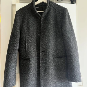 Grå kappa från Selected Homme / M - Snygg grå kappa i ull från Selected Homme i ett klassiskt snitt. Kappan har en stilren design med knappar framtill och diskreta fickor. Perfekt för kyligare dagar. Nyskick. Storlek M