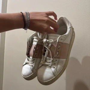 Valentino sneakers i vitt och rosa - Snygga Valentino sneakers i vitt med rosa detaljer. Skorna har snörning och ikoniska nitar på sulan. Perfekta för en stilren look. Dom är äkta!!! Kommer inte med någon box! 