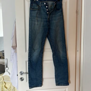 Levis 501 jeans - Klassiska Levis 501 jeans i blå denim med knappgylf. De har en rak passform och är tillverkade i slitstarkt jeanstyg. Perfekta för en avslappnad stil.