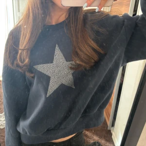 Mörkblå sweatshirt med stjärndetalj - Säljer en mörkblå sweatshirt med en glittrig stjärna på framsidan. Tröjan har långa ärmar och ribbade muddar vid ärmslut och nederkant. Perfekt för en avslappnad stil.