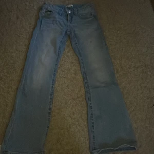 Blå jeans från Gina Tricot - Säljer ett par klassiska blå jeans från Gina Tricot. De har en bootcut/flared passform och är tillverkade i denim. Jeansen har fickor både fram och bak samt knappar på bakfickorna för extra stil. Perfekta för en avslappnad look.