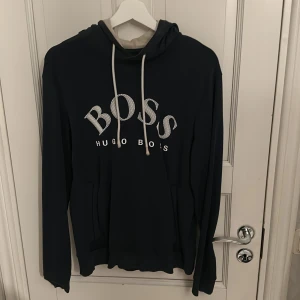 Mörkblå hoodie från Hugo Boss - Säljer en stilren mörkblå hoodie från Hugo Boss med vit logga på bröstet. Passar bra för en avslappnad look.