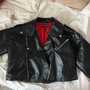 Svart skinnjacka från PrettyLittleThing - Snygg svart skinnjacka från PrettyLittleThing med röd insida. Jättebra skick då den knappt är använd. Pris går att diskutera😊