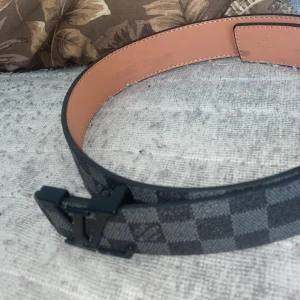 Rutig bälte med svart spänne - Snyggt bälte med ett rutigt mönster i grått och svart. Bältet har ett stilrent svart spänne och är perfekt för att ge en extra touch till din outfit.