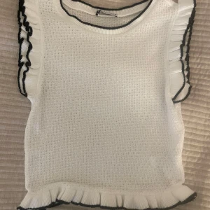 Vit stickad topp från Zara - Säljer en supersöt vit stickad topp från Zara med svarta detaljer. Toppen har volanger längs ärmarna och en ribbad kant vid halsen. 