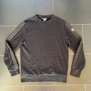 Svart tröja från Colmar - Snygg svart tröja från Colmar med ribbade detaljer längs ärmarna. Perfekt för en stilren look. Tröjan har en rund halsringning och är tillverkad i ett mjukt material.