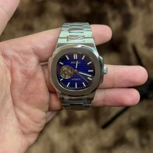 Automatisk klocka med blå urtavla - Snygg automatisk klocka från Seiko med en djupblå urtavla och silverfärgad boett. Klockan har ett öppet urverk som ger en cool inblick i mekaniken. Armbandet är i rostfritt stål och ger en elegant touch. Perfekt för den som gillar stilrena accessoarer.