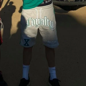 Grå shorts med tryck - Snygga grå shorts med texten 'Loyalty' tryckt i en cool stil på framsidan. De har en bekväm passform med snörning i midjan för justering. Perfekta för en avslappnad stil.