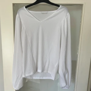 Vit v-ringad blus - Säljer en stilren vit blus med v-ringning och långa ärmar. Perfekt för en elegant och avslappnad look. Blusen har en lätt textur och faller fint.