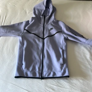 Ljuslila hoodie från Nike - Säljer en snygg ljuslila Nike tech. Jackan har svarta detaljer och en ficka på armen. Använd fåtal gånger inga synliga skador. Säljer för att den är för liten. Kan diskutera pris. Köpt för 1300.
