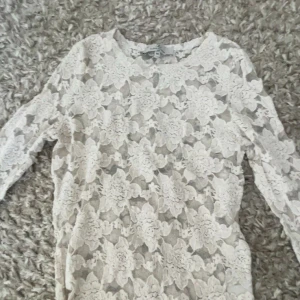 Vit spetsblus - Kom privat för mer bilder, Säljer en elegant vit spetsblus med blommigt mönster. Blusen har trekvartsärmar och en rund halsringning. Perfekt för en stilren look.