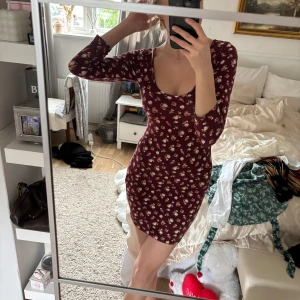 Vinröd blommig miniklänning - Säljer en söt vinröd klänning från Forever 21 med blommigt mönster. Klänningen har en tight passform och trekvartsärmar, perfekt för både vardag och fest. Den är tillverkad i ett mjukt och bekvämt material.