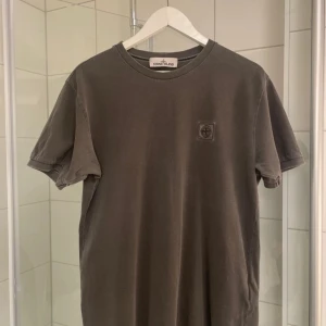 Grå t-shirt från Stone Island - Säljer en stilren grå t-shirt från Stone Island med korta ärmar och en diskret logga på bröstet. Perfekt för en avslappnad look.