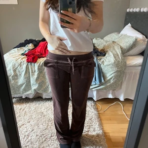 Bruna mjukisbyxor från Juicy Couture - Säljer ett par bruna mjukisbyxor från Juicy Couture. Byxorna har en snörning i midjan och bakfickor med knappar. Perfekta för en avslappnad stil.
