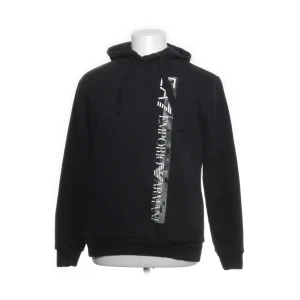 Svart hoodie från Emporio Armani - Snygg svart hoodie från Emporio Armani med en vertikal logotyp i vitt på framsidan. Den har en klassisk huva med dragsko och långa ärmar. Perfekt för en stilren och bekväm look.
