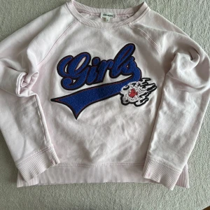 Ljusrosa sweatshirt från Zadig & Voltaire - Säljer en ljusrosa sweatshirt från Zadig & Voltaire med ett stort blått och svart tryck med texten 'Girls' och en cool detalj på framsidan. Tröjan har långa ärmar och ribbade muddar vid ärmslut och nederkant. Perfekt för en avslappnad stil!