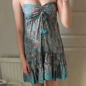 Blommig  klänning - Säljer en söt blommig klänning i turkos med rosa och beige detaljer. Axelbanden går att vika ner om man vill. Köpt på marknad i Italien. 