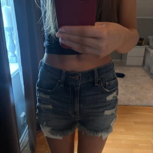 Mörkblå jeansshorts med fransar - Säljer ett par mörkblå jeansshorts med fransiga kanter och slitna detaljer från hollister!! Nyskick! (har vanligtvis xs, lite stora på mig)