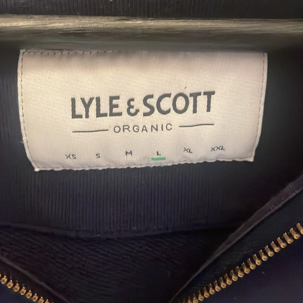 Säljer mörkblå hoodie från Lyle & Scott med dragkedja och huva. Den har en liten gul logga på bröstet och praktiska fickor framtill. Perfekt för en avslappnad stil.. Neuletakit & Villapaidat.