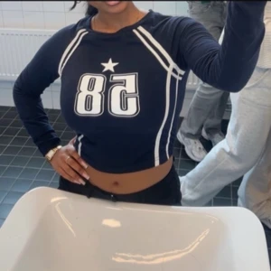 Mörkblå långärmad topp med tryck - Säljer en mörkblå långärmad topp med ett stort vitt tryck av siffran 58 och en stjärna på framsidan. Toppen har en sportig look med vita detaljer längs ärmarna och sidorna. 