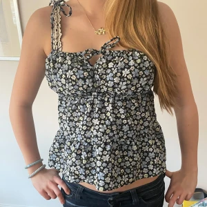 Blommig topp med knytband - Säljer en söt blommig topp med knytband vid axeln. Jättefin till sommaren och våren