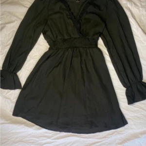 Svart klänning från Emery Rose - Elegant svart klänning från Emery Rose med v-ringad design och spetsdetaljer. Klänningen har långa ärmar och en smickrande passform med markerad midja. Perfekt för en stilren look.