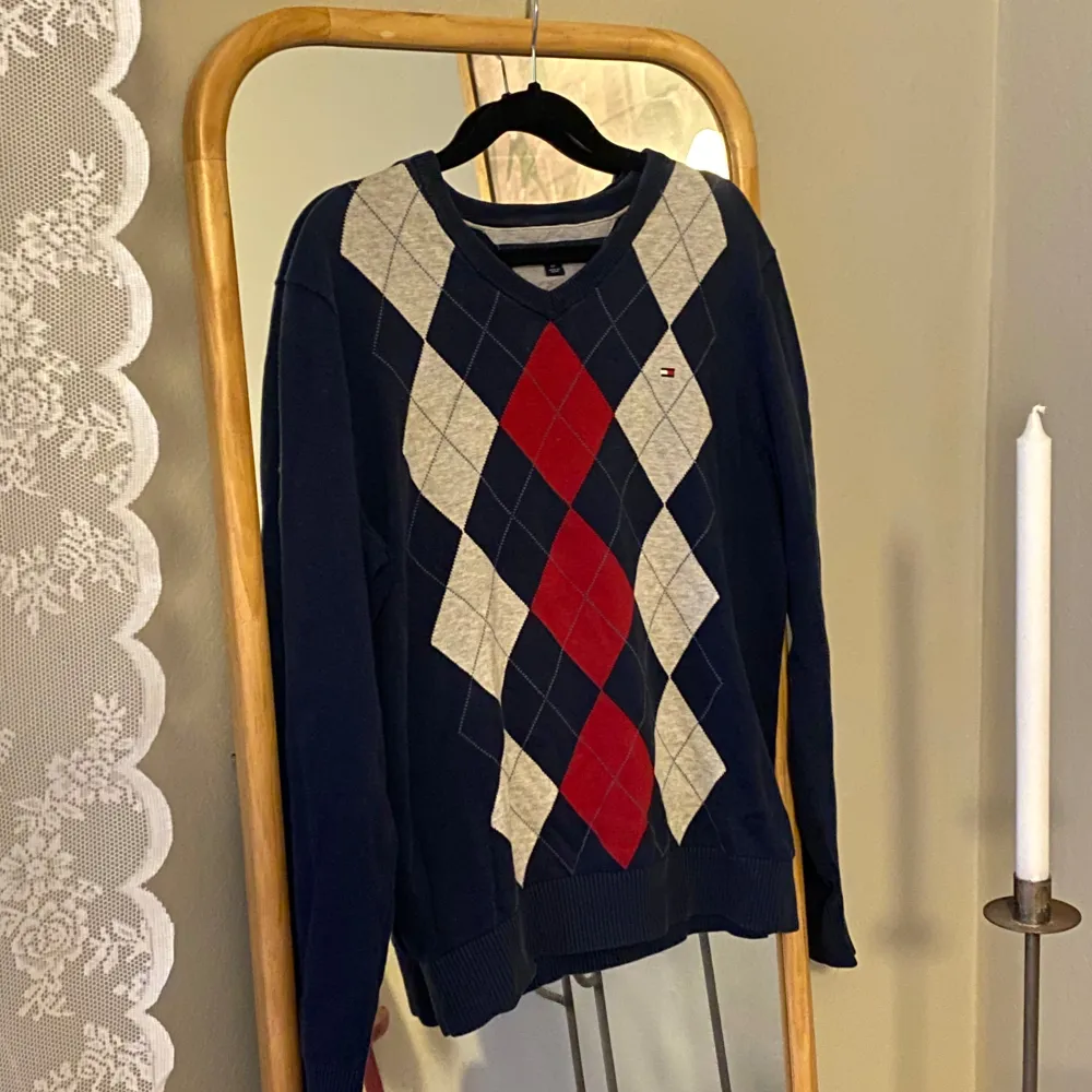 Snygg tröja från Tommy Hilfiger med ett klassiskt argylemönster i blått, rött och vitt. Tröjan har en v-ringad hals och långa ärmar, perfekt för en stilren look. Passar bra till både jeans och chinos.. Neuletakit & Villapaidat.
