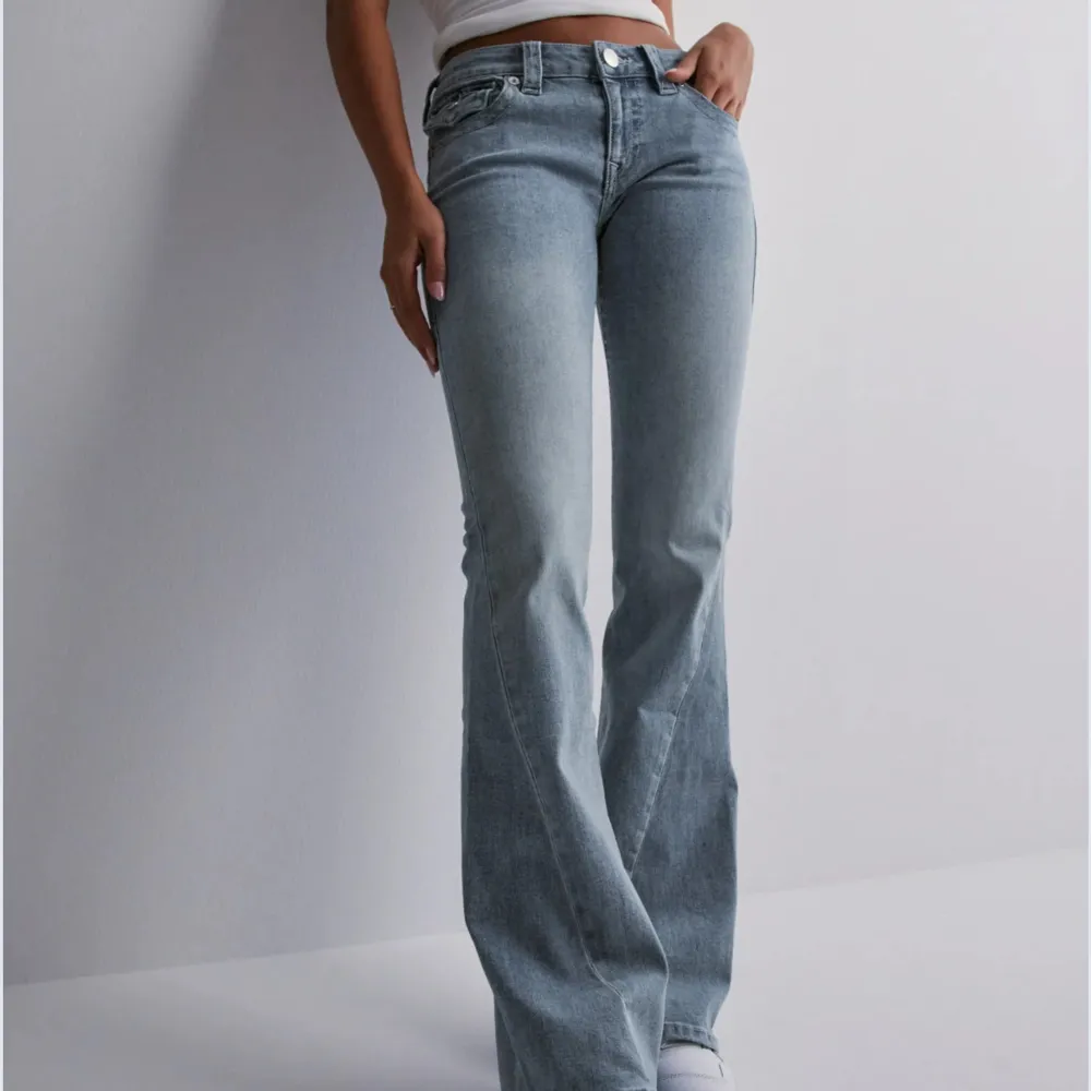 Snygga ljusblå bootcut jeans med låg midja och klassisk femficksdesign. Jeansen har dekorativa sömmar och knappar på bakfickorna. Perfekta för en avslappnad stil.. Farkut & Housut.