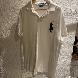 Vit pikétröja från Ralph Lauren - Säljer en klassisk vit pikétröja från Ralph Lauren med den ikoniska broderade loggan på bröstet. Tröjan har korta ärmar och en stilren krage. Perfekt för en avslappnad men ändå stilren look. Passar bra till både jeans och chinos.