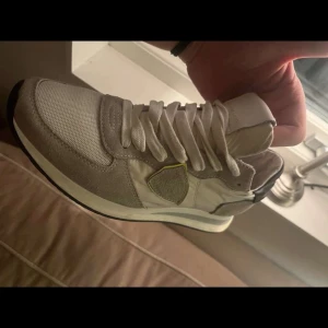 Sneakers från Philippe Model - Snygga sneakers från Philippe Model i en stilren design. Skorna är vita med grå detaljer och har en rund tå. De är tillverkade i en kombination av skinn och syntetmaterial. Perfekta för en casual look.