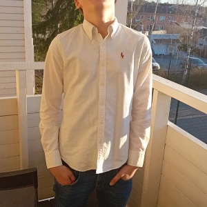 Vit skjorta från Ralph Lauren - Säljer en klassisk vit skjorta från Ralph Lauren med broderad logga på bröstet. Skjortan har långa ärmar och knappar framtill. Perfekt för en stilren look.