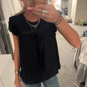 mörkblå topp - Svart blus från Shein i storlek M med broderade hål och volangärmar. Toppen har en luftig passform och fina detaljer upptill med små hål och lätt rynkning. Perfekt till jeans eller kjol för en chill och snygg look.