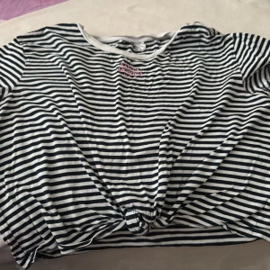 Randig croppad topp med knyt - Säljer en svartvit randig topp från Monki med korta ärmar och knyt framtill. Toppen har en croppad passform och är gjord i mjuk bomull. Perfekt för dig som gillar avslappnad och trendig stil.