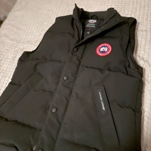 Svart dunväst från Canada Goose - Svart äkta dunväst från Canada Goose med klassisk röd och vit logga på bröstet. köpt för 4500kr Perfekt för kalla dagar och sitter jätte bra