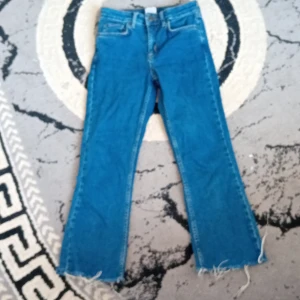 Blå jeans med råa kanter - Säljer ett par klassiska blå Levi's jeans med raka ben och råa, fransiga benslut för en cool och avslappnad vibe. Jeansen har fem fickor och en läderpatch bak i midjan. Perfekta för dig som gillar en lite edgy stil.