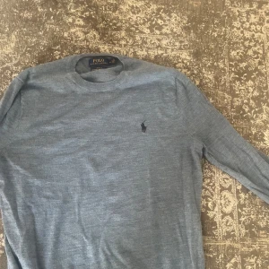 Grå stickad tröja från Polo Ralph Lauren - Snygg grå stickad tröja från Polo Ralph Lauren med klassisk rund hals och diskret logga broderad på bröstet. Perfekt för dig som gillar stilrena och tidlösa plagg. Långärmad och mjuk i materialet, passar till jeans eller chinos.