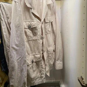 Beige manchester overshirt oscar jacobson - Snygg beige overshirt i manchester med fyra stora fickor framtill och knappar hela vägen. Jackan har klassisk krage och lång ärm, perfekt för lager-på-lager. Stilren och enkel att matcha med jeans eller chinos.