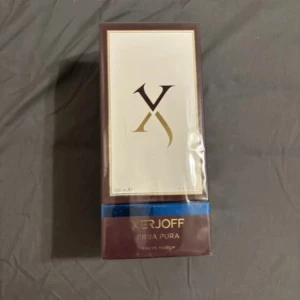 Xerjoff Erba Pura Eau de Parfum 100ml - Lyxig parfym från Xerjoff, Erba Pura, i en elegant brun och vit kartong med guldiga detaljer. Flaskan rymmer 100 ml Eau de Parfum och har en exklusiv känsla med stilren design och blå accent på förpackningen.