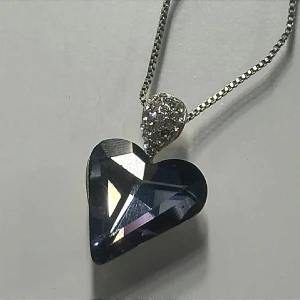 Halsband med blå hjärtformad kristall - Snyggt halsband med en blå hjärtformad äkta kristall som hänge. Ovanför hjärtat sitter en dekoration med glittriga stenar. Rostas ej